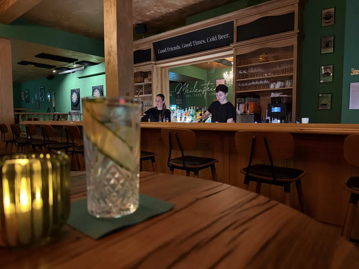 Die Theke der Bar Meilenstein mit Holzvertäfelung, grünen Wänden und beleuchtetem Flaschenregal